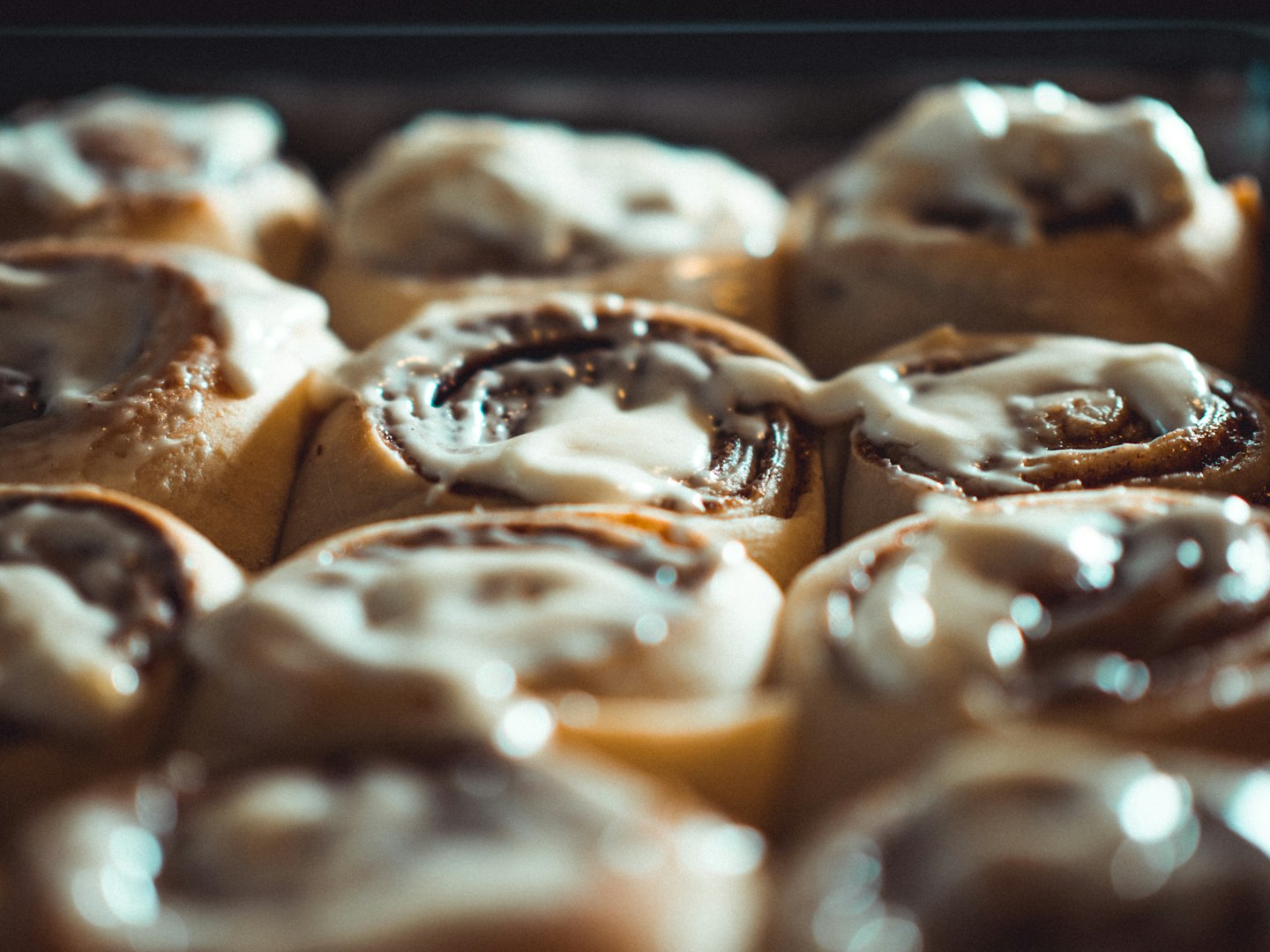Freshly baked cinnamon rolls with white icing in a dark pan.