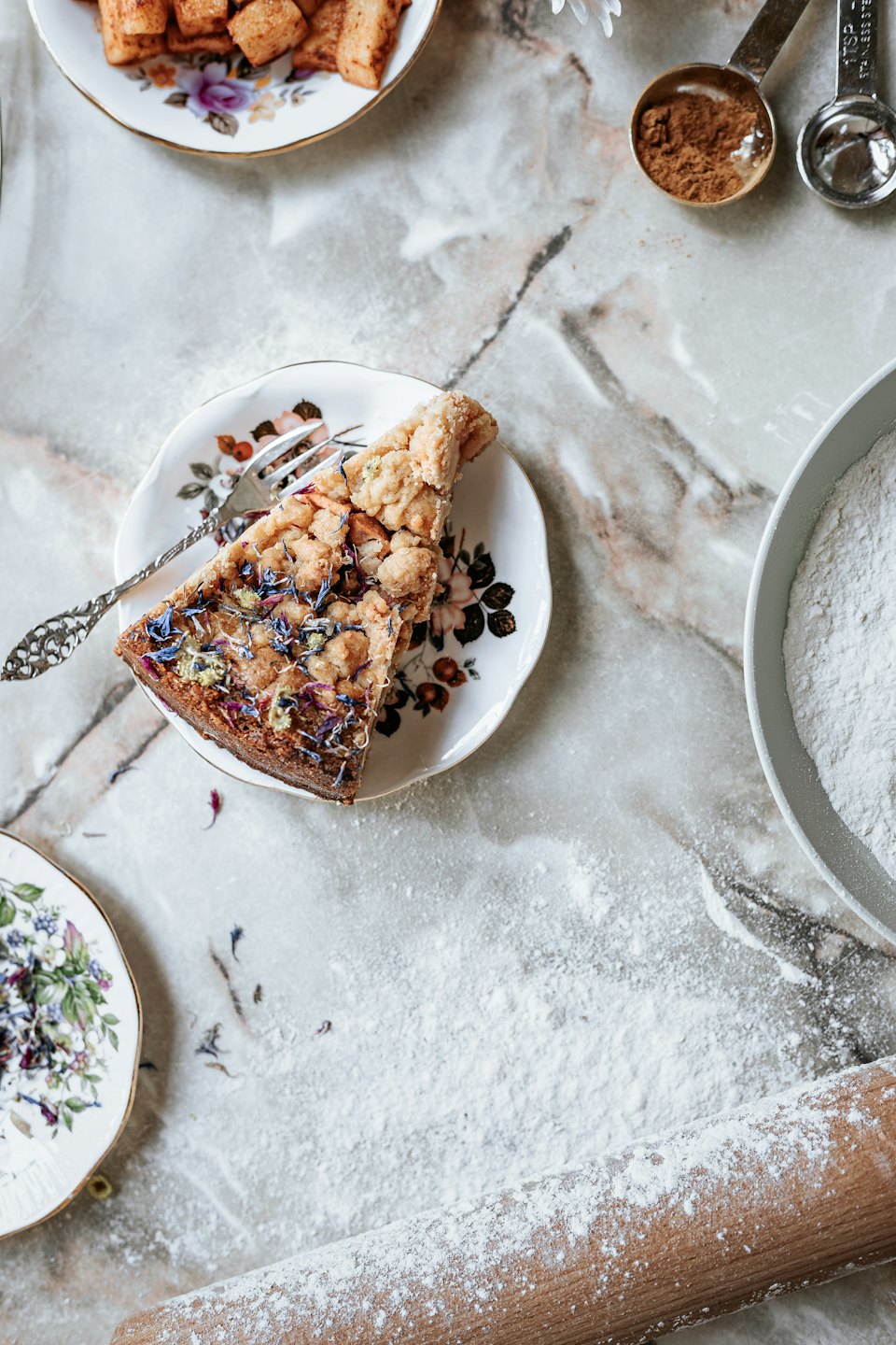 Slice of crumble cake with edible flowers on a floral plate.
